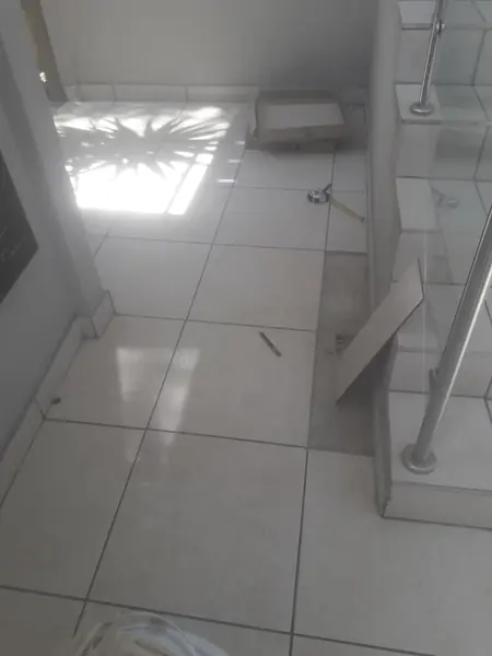 Handyman job: floor tile lifted beside stair rail, tape measure and tools