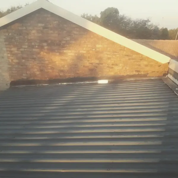 Before. Waterproofing job: corrugated roof meeting brick gable wall, bare metal, evening light