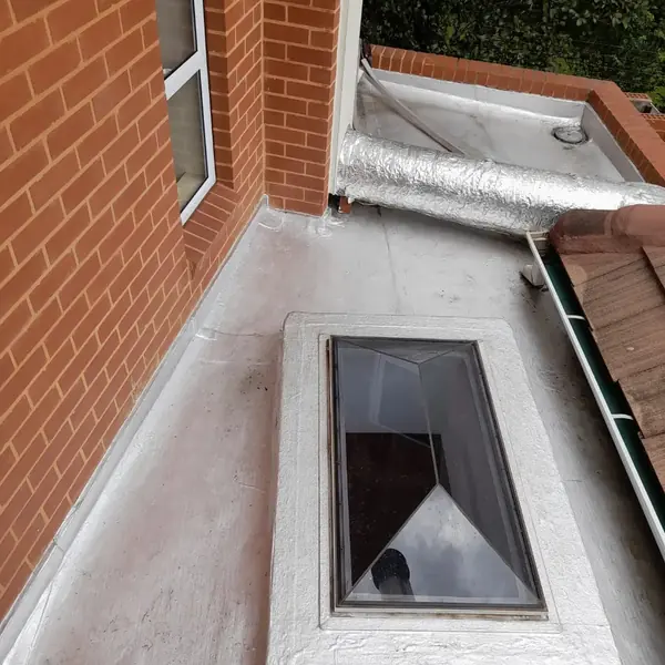 Waterproofing job: grey sealed flat roof, skylight and foil duct beside brick wall